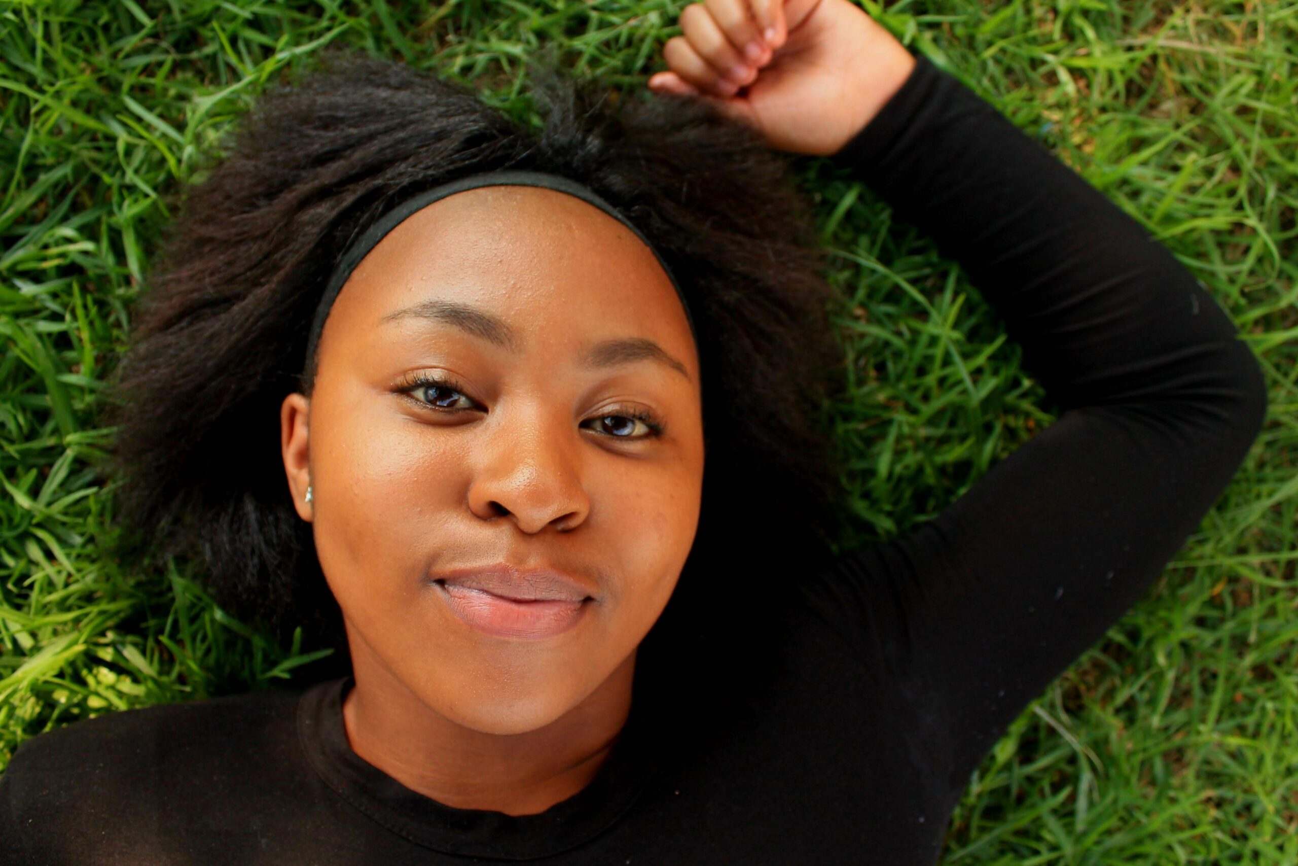 A serene portrait of a woman with afro hairstyle relaxing on a green lawn.